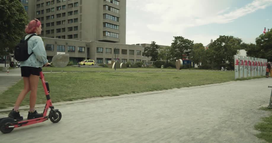 A woman rides an electric scooter past people walking on a trail in a park