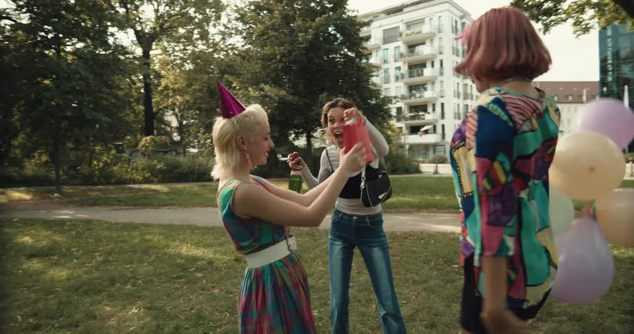 Group of friends wearing party hats greet each other and celebrate with balloons in the park