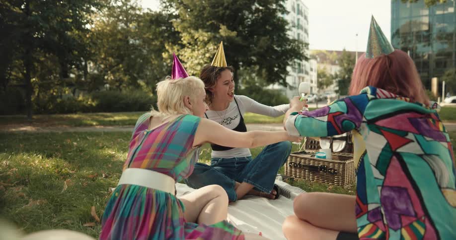 Three women are sitting in a park celebrating and drinking champagne