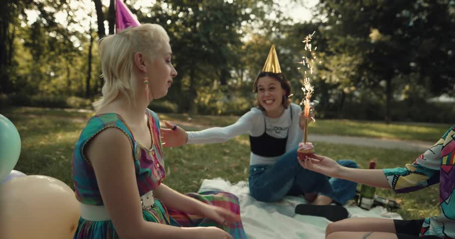 A group of women celebrate a birthday outside with a large candle in a cupcake