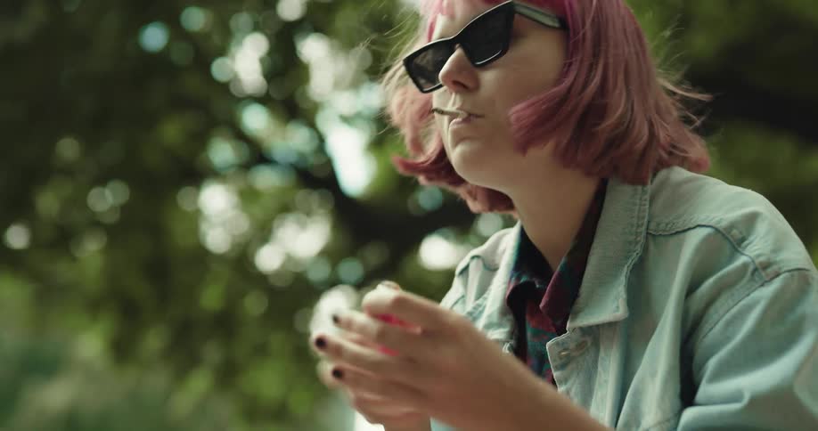 A woman is outside near trees and smoking a cigarette