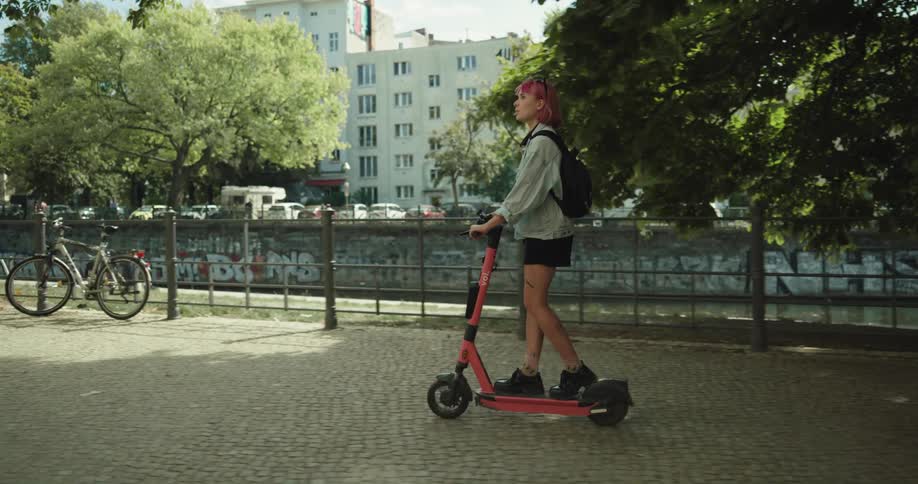 A young woman rides an electric scooter through a park