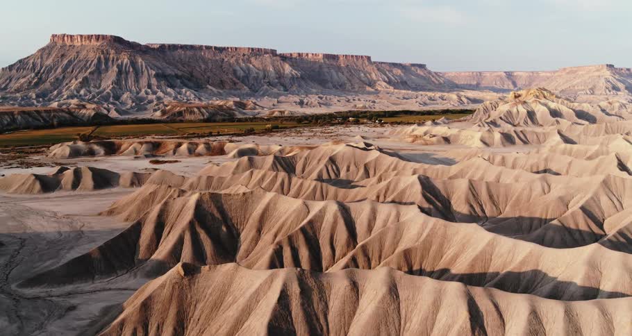 Aerial view of desert badlands as the sun shines on mountains and mesa