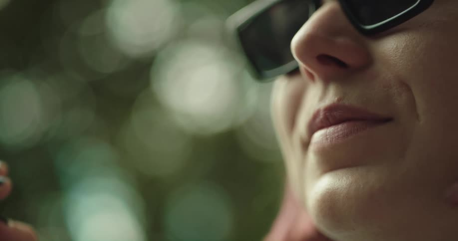 Woman with pink hair and sunglasses smokes a cigarette in the park