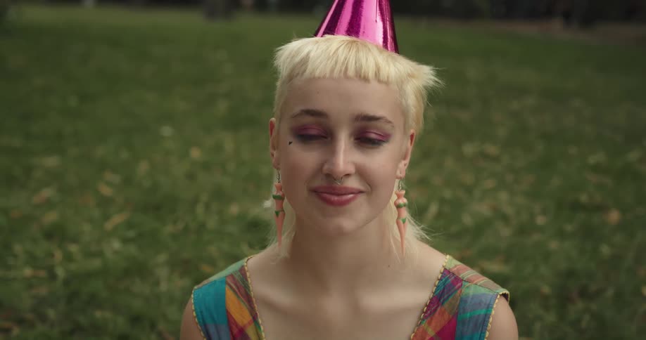Young short haired blonde woman wearing a party hat while sitting on the grass at the park