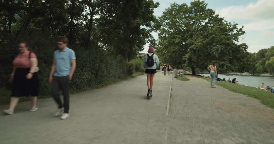 A woman rides a scooter on a pathway at a park near the river