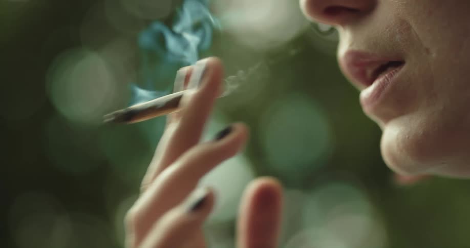 Shade wearing woman with brightly dyed hair smokes a hand rolled cigarette