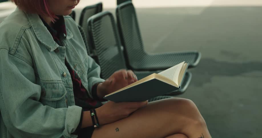 A woman is sitting on a chair and reading a book outdoors