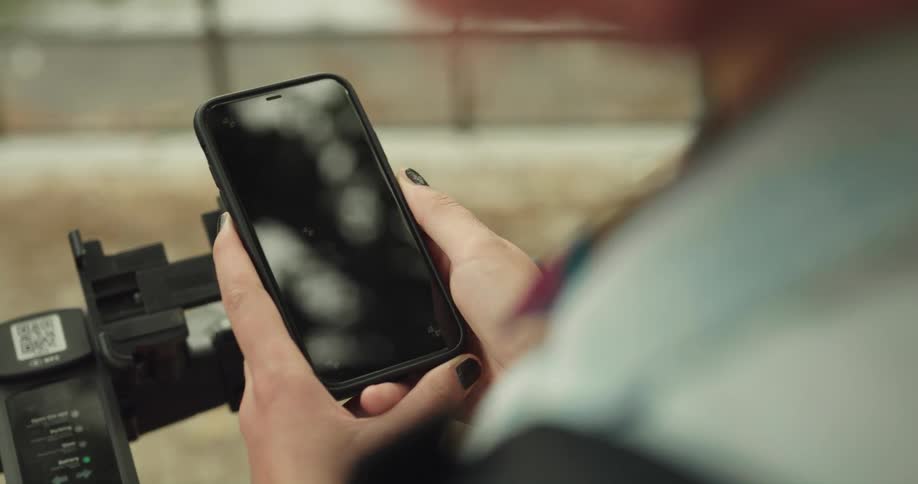 A girl wearing black fingernail polish is holding her phone with both hands as she moves her thumb across the screen