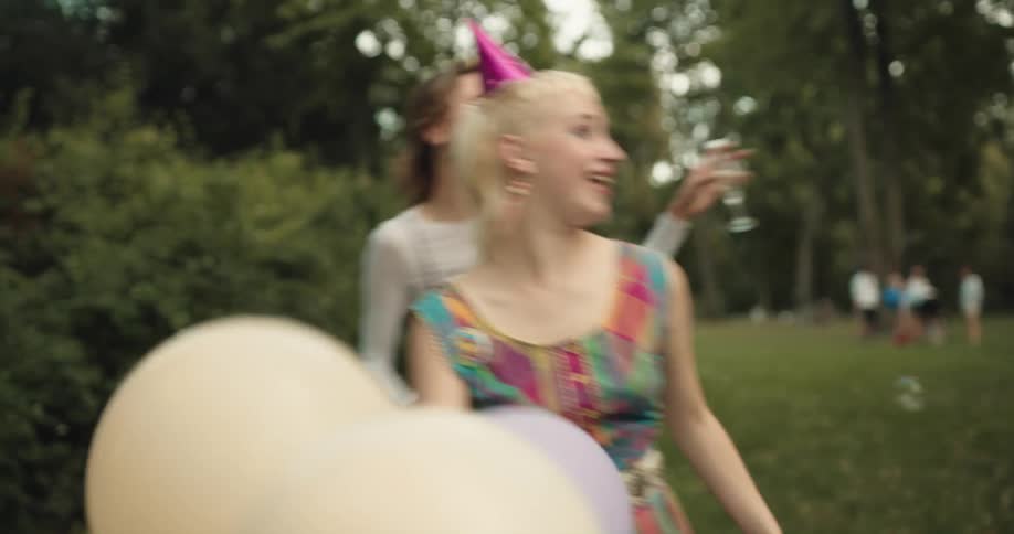 A group of friends dance around their yard blowing bubbles and playing with party balloons