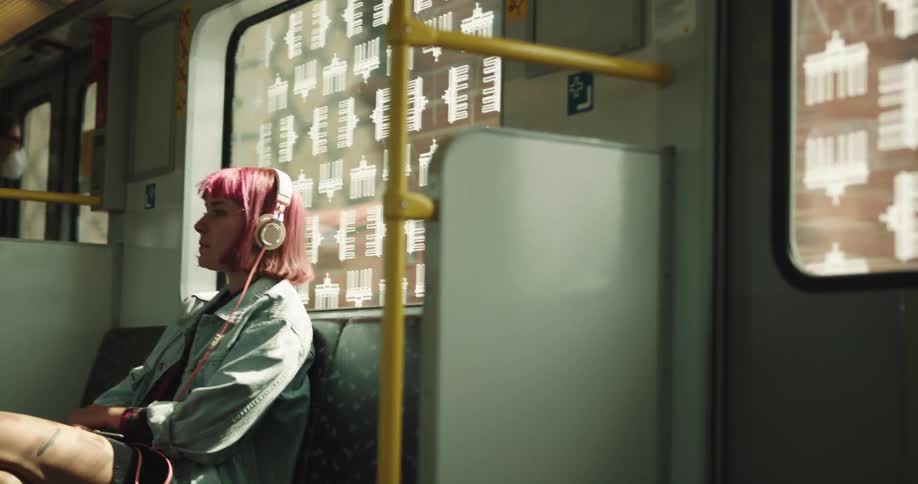 A teenage girl is sitting in a seat on a train with headphones on her head