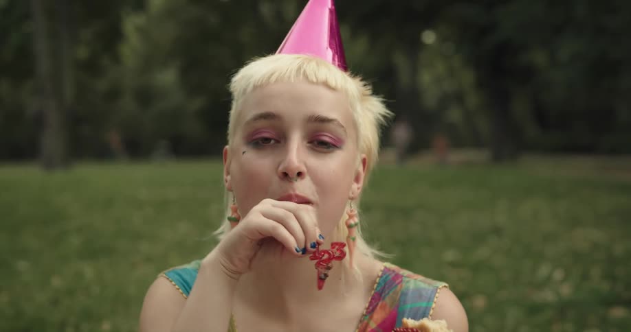 A woman in a park laughs as she takes large bites from a slice of cake