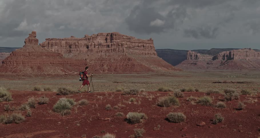Man with a backpack hikes over a hill near the mountains in the badlands