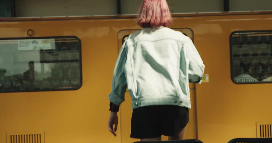 A teenage girl is sitting at a train station waiting for her train and when it stops she gets up and walks on when the door opens