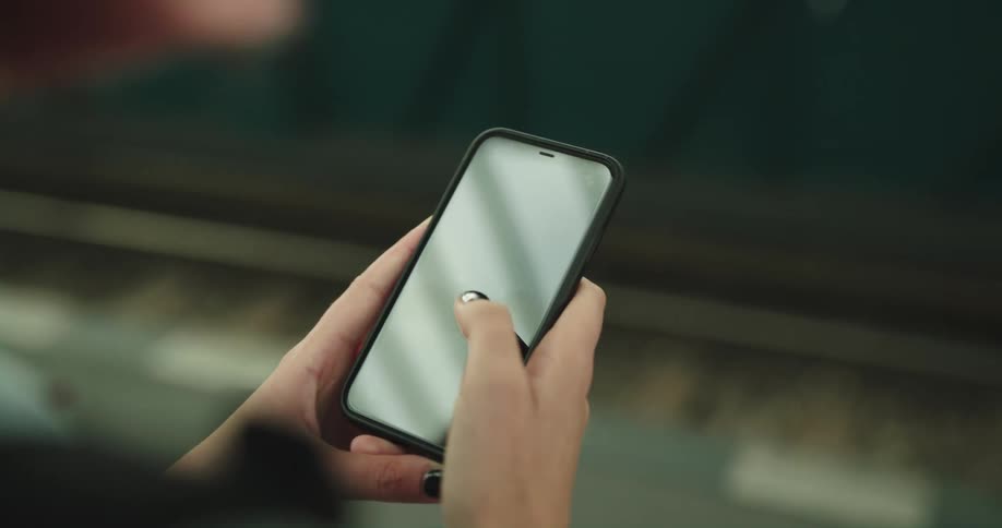A woman scrolls through her smartphone while waiting for a train