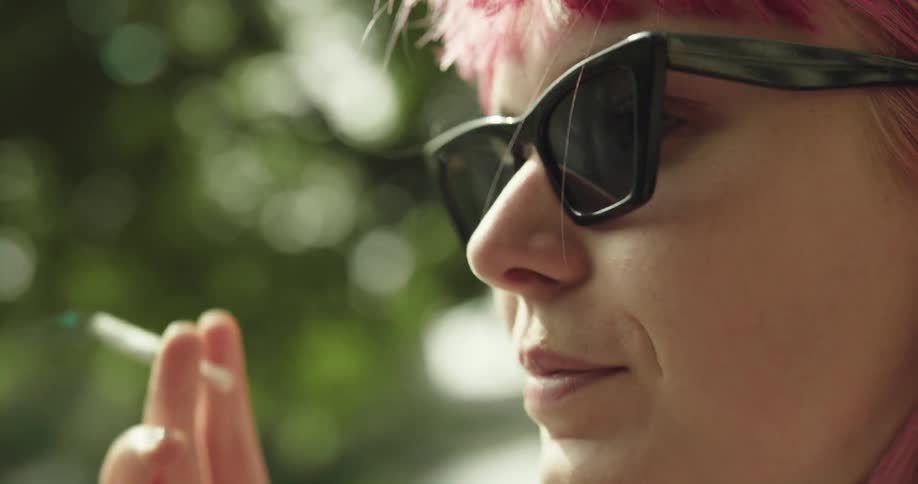 Woman with oink hair sunglasses and denim jacket lights cigarette smoking
