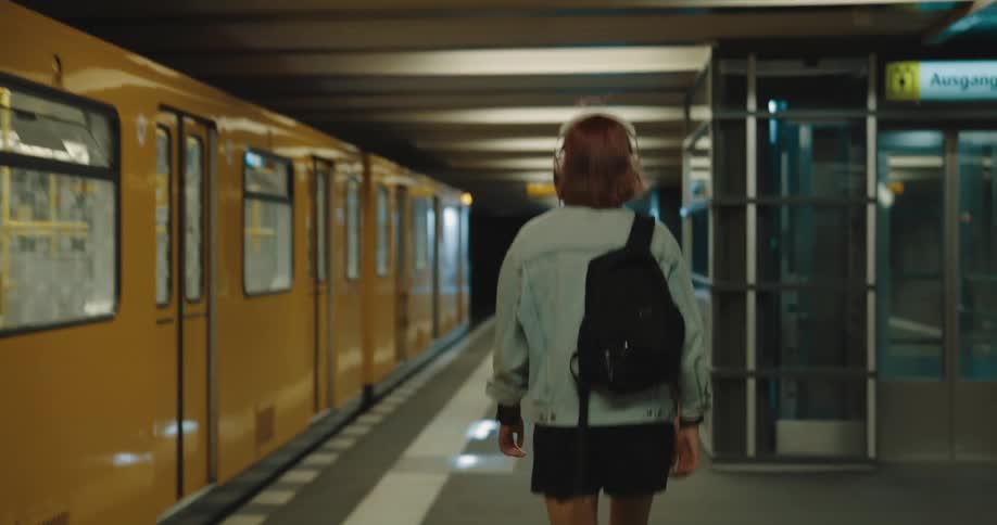 A woman wearing headphones walks through a subway station towards the exit