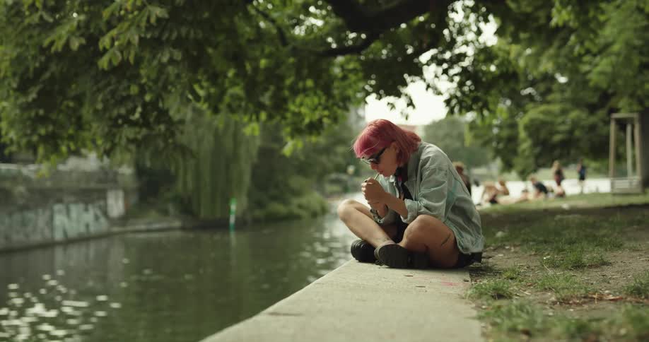 A woman is smoking at a public park by water