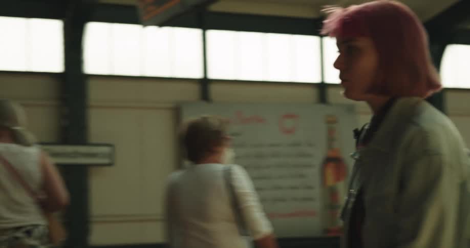 A woman with pink hair gets off the train and heads toward the up escalator