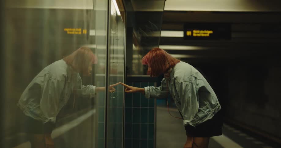 A woman stands in front of a schedule inside a train station and then checks her cell phone