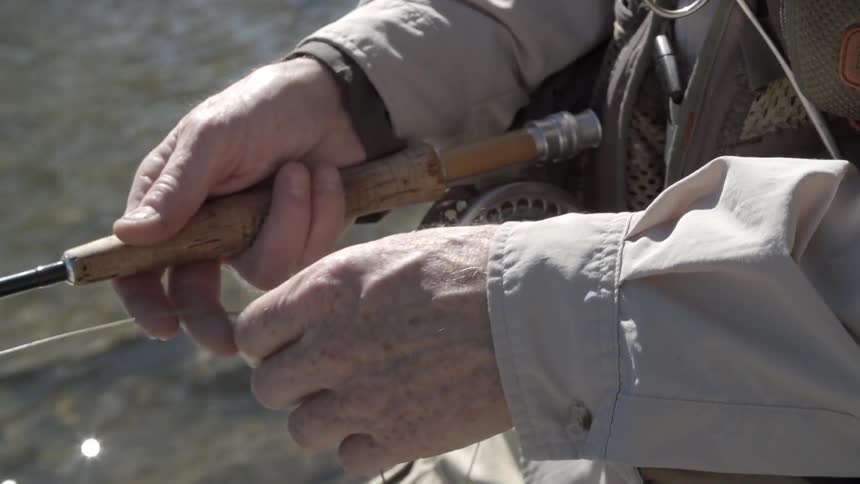 Man threads line on his fishing pole while standing in water