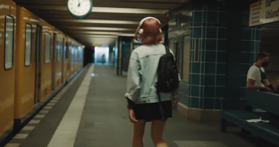 A young woman sitting on a subway exits the train and begins to walk towards the staircase leading to the surface