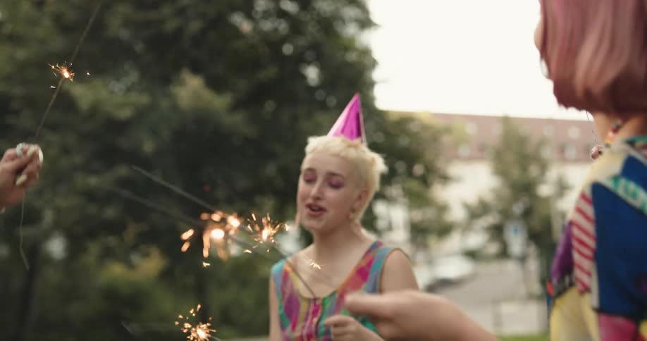 Female friends dance and wave sparklers around in park