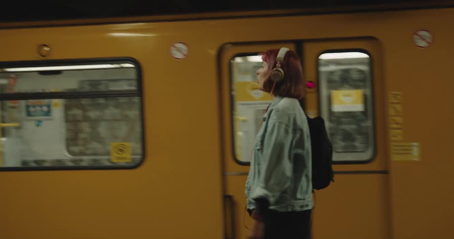 A woman is walking in a train terminal and listening to music