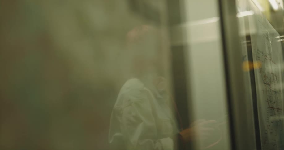 Reflection of a woman with pink hair reading a map on a subway billboard