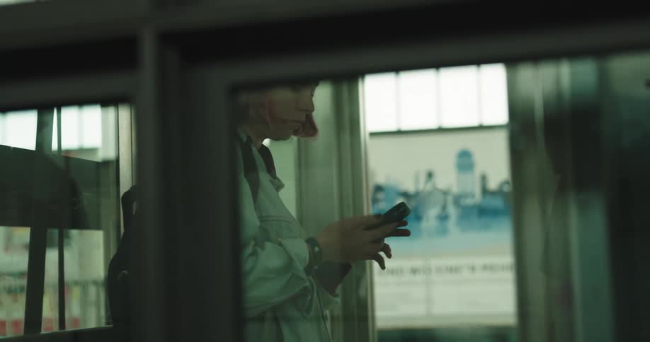 A woman gets on an elevator and looks at her cell phone