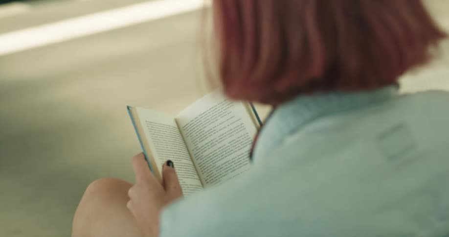 A woman is sitting outdoors and reading a book