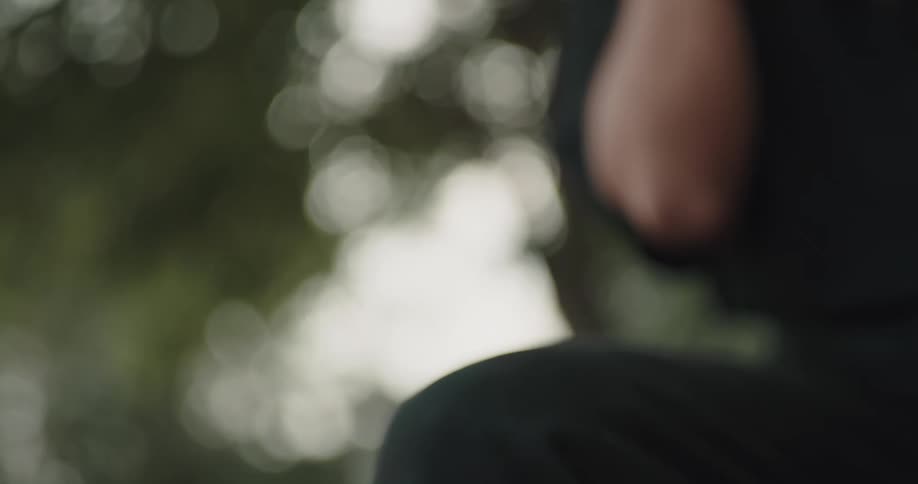 A man is sitting outside near trees and smoking a cigarette