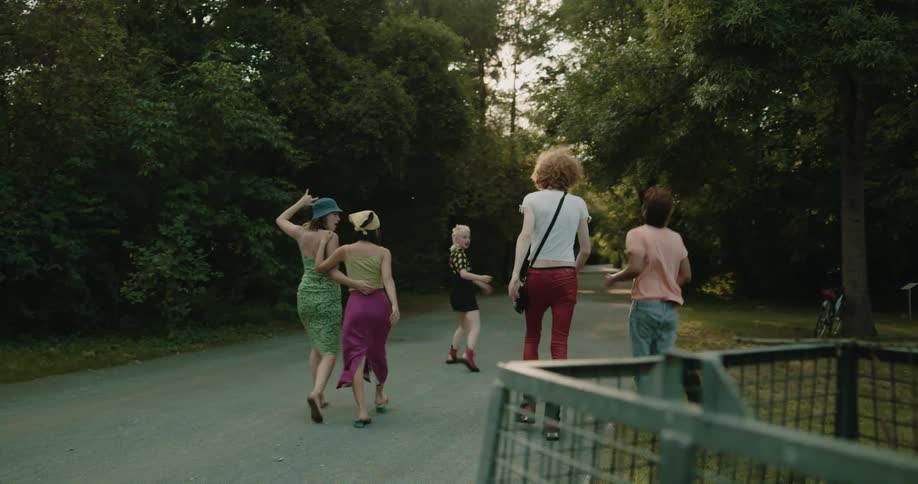 A group of young adults through a large trash bag into a trash can in a park