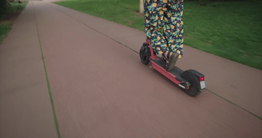 A woman smiles as she rides an electric scooter on a park path