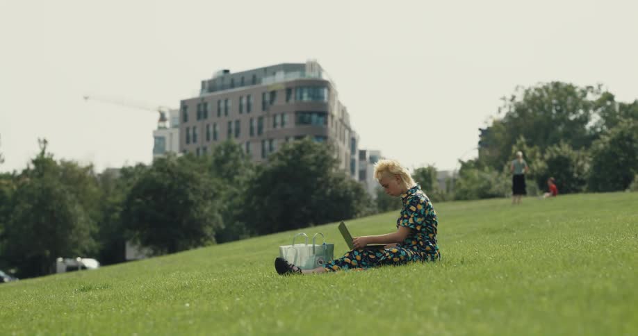 A woman sits down on the grass in the park