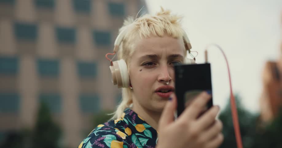A woman stands outside in a city and moves her phone around while she talks