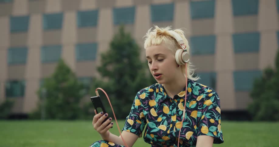 A woman is sitting on a lawn in front of a building and talking on the phone