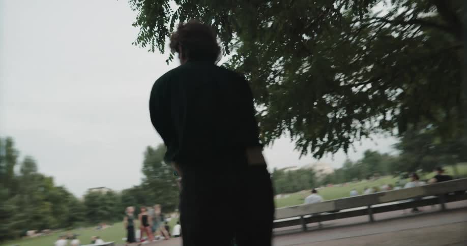 A woman and man dance together atop a bench in a public park during the day