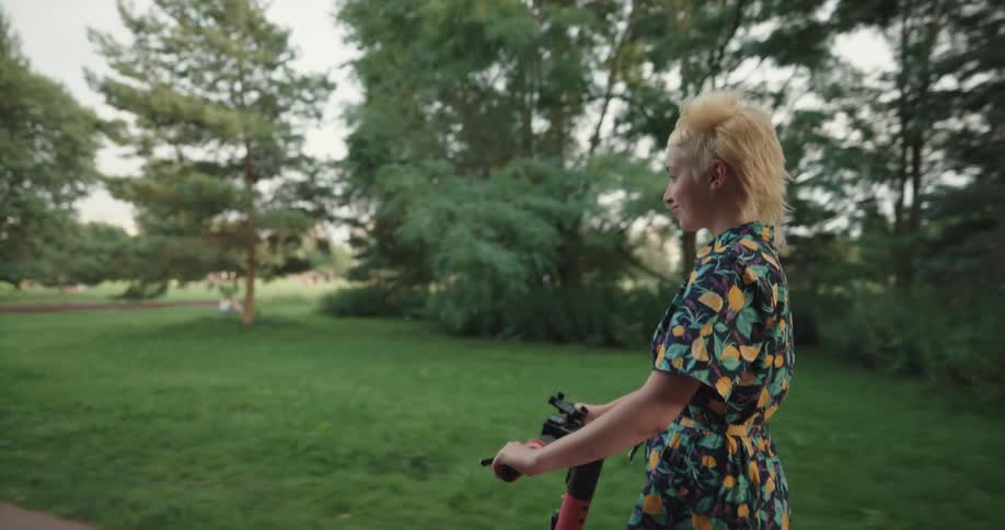 A woman smiles as she rides an electric scooter on a public park path