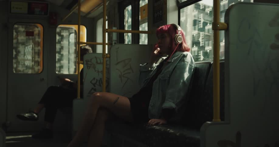 A teenage girl is sitting in a seat on a train with headphones on her head