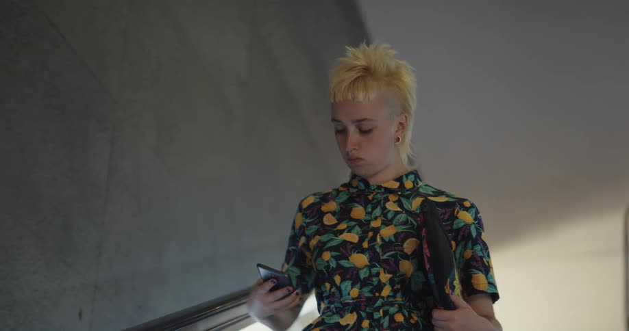 A woman is looking at her cell phone while going down the escalator