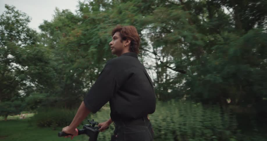 A man rides an electric scooter on a park path passing people walking