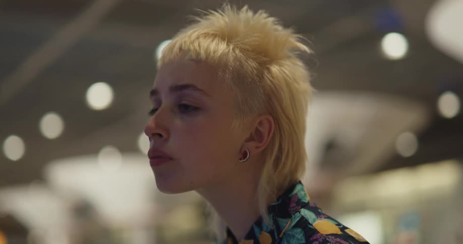 Young short haired blonde woman in colorful clothes looking at goods on a big department store