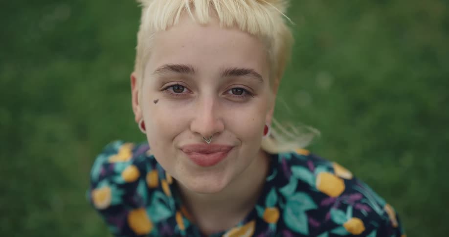 A woman is smiling and sitting in the grass during the day time