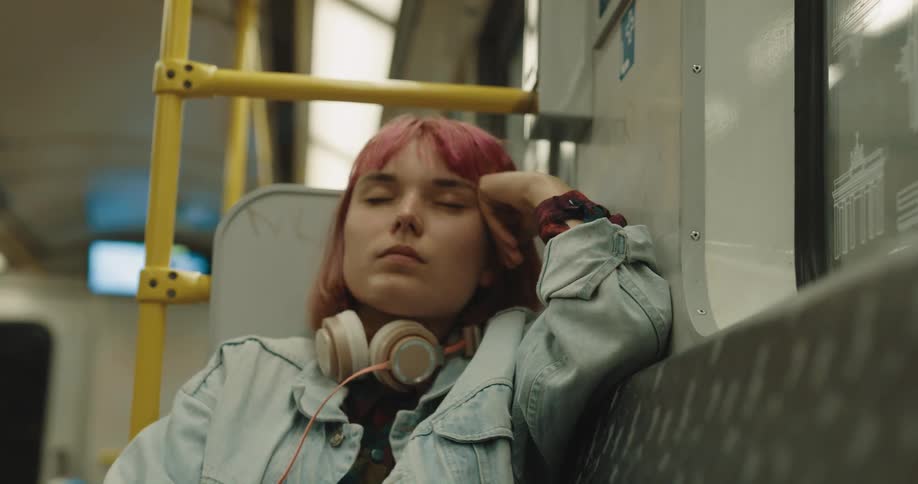 Woman sitting in train car leans head on hand and closes her eyes