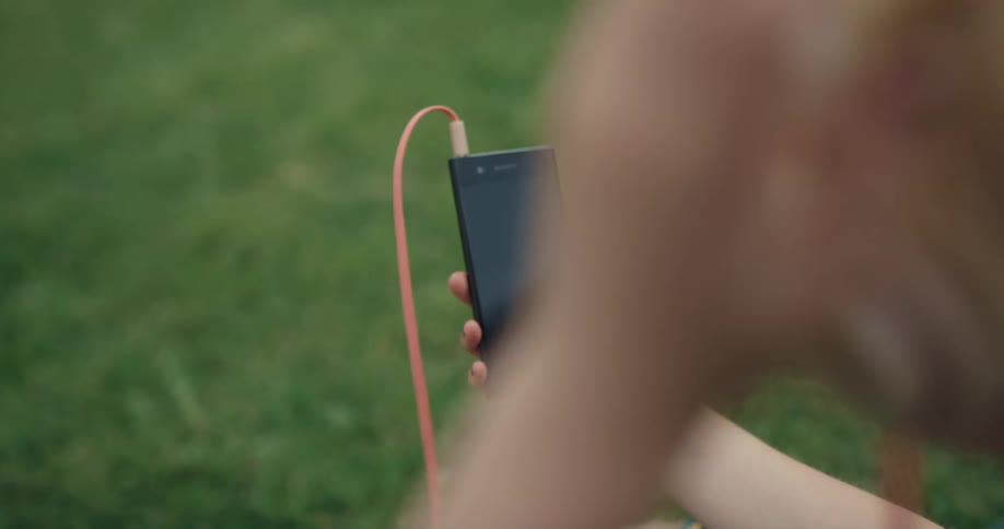 A female is sitting in the grass and looking at a cell phone