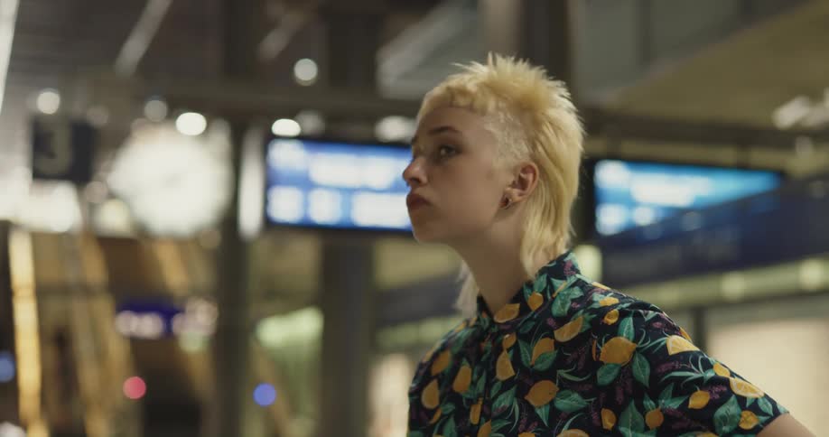 A woman stands waiting for the subway looking at her cell phone and looking at her surroundings