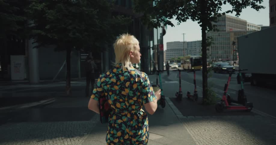 Young short haired blonde woman wearing a colorful dress walking on the sidewalk in the city