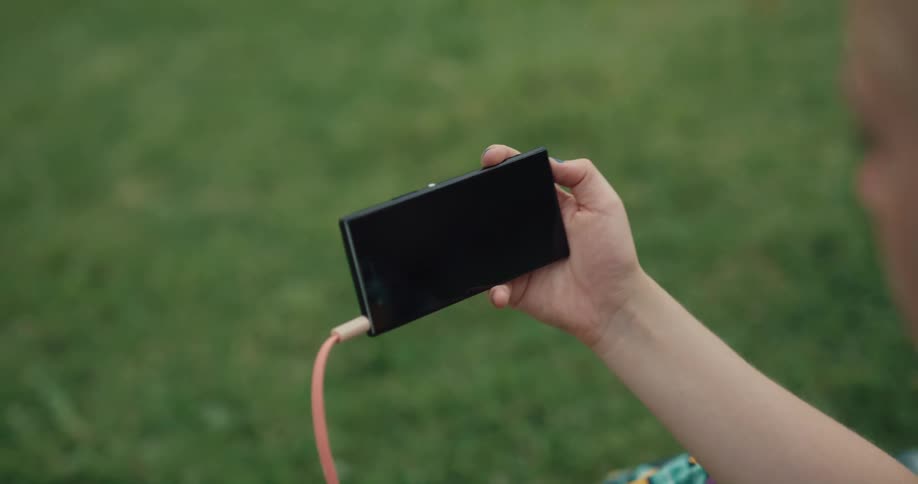 A woman is sitting outdoors and listening to music on her cell phone