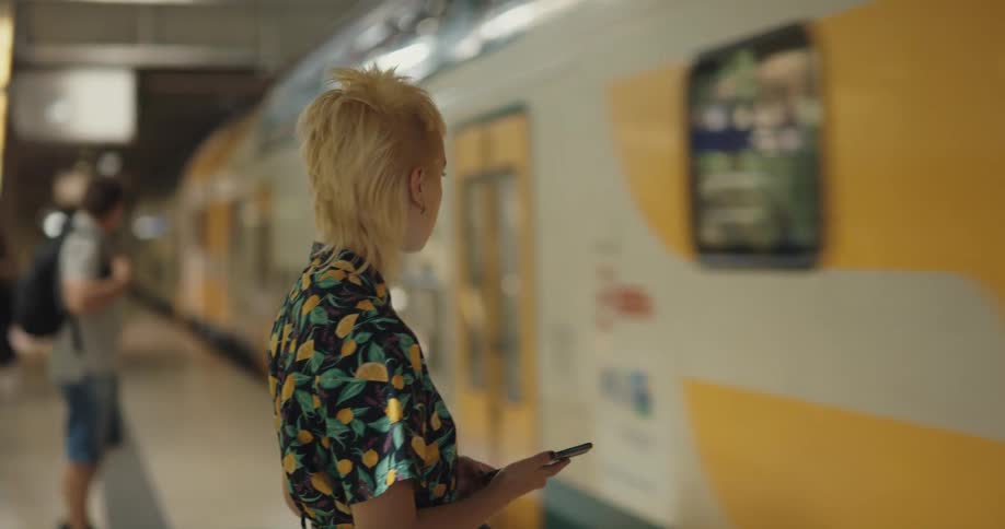 A woman stands waiting for the subway looking at her phone